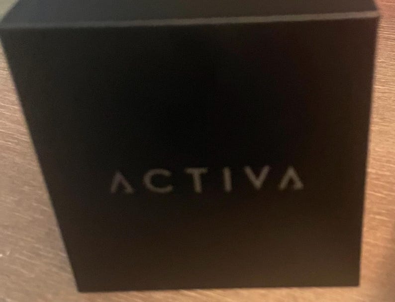 May include: A square black box with the word ACTIVA printed in a light gray, sans-serif font centered on the front face. The box has a smooth, matte finish and sharp, clean edges, presenting a simple and uniform appearance throughout the object.