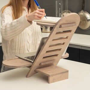 May include: A wooden laptop stand with a built-in shelf for a notebook. The stand is light brown and has a natural wood grain finish. The stand is angled to provide ergonomic support for a laptop.