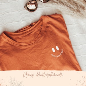 Könnte beinhalten: Ein orangefarbenes T-Shirt mit einem weißen Smiley und dem Text "NOPE. NOT TODAY!" auf der Vorderseite.