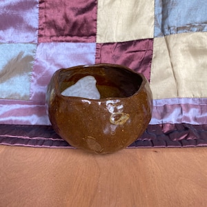 May include: A brown ceramic bowl with a white glaze on the inside. The bowl has a rounded shape and a slightly uneven rim.