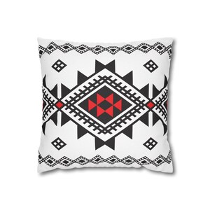 Può includere: Un cuscino quadrato con sfondo bianco e un motivo geometrico centrale a rombi in nero e rosso. Il design presenta bordi neri seghettati, piccoli quadrati neri negli angoli e un bordo orizzontale composto da rombi neri.