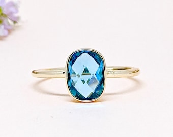 May include: A gold ring with a cushion-cut blue topaz gemstone.