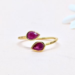 Op de afbeelding: Een gouden ring met twee druppelvormige robijnstenen. De ring is ontworpen om om de vinger te wikkelen.