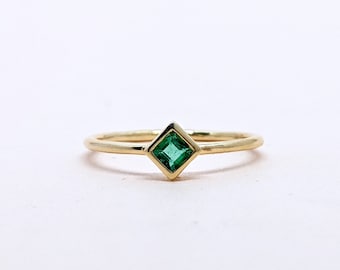 May include: A gold ring with a square emerald green gemstone set in a gold bezel.