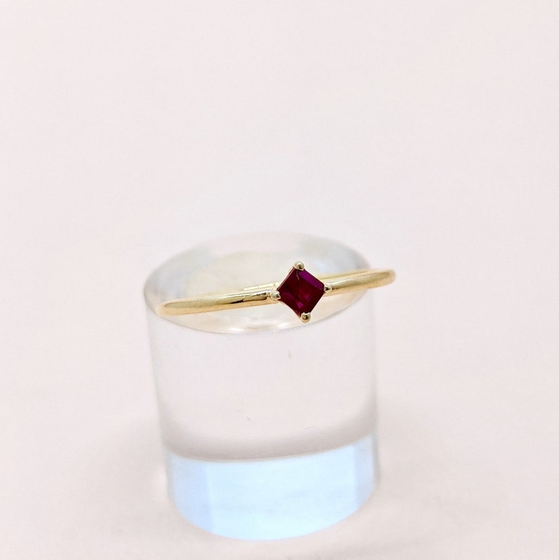 May include: A gold ring with a small, square-shaped ruby gemstone.