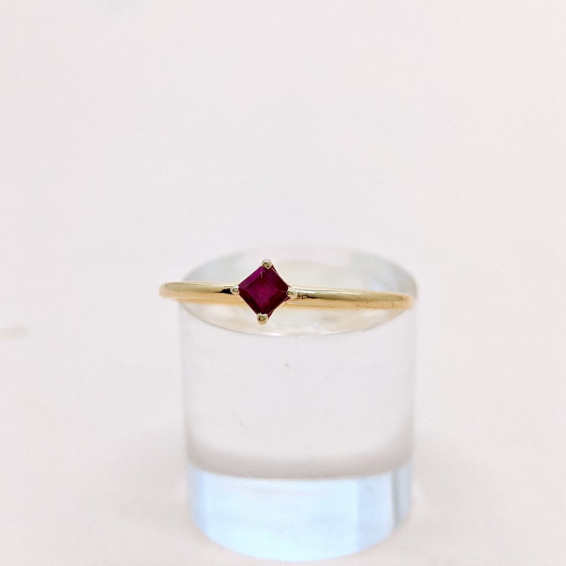 May include: A gold ring with a small, square-shaped ruby gemstone.