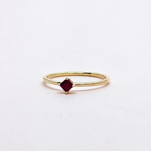 May include: A simple gold band ring with a small, square-shaped ruby gemstone.