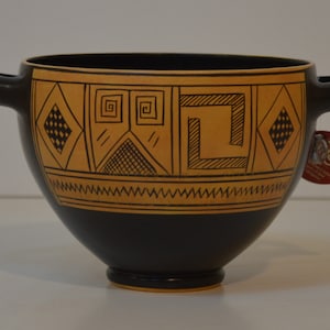 Può includere: Una ciotola in ceramica nera con due manici e un design geometrico in oro. Il design presenta quadrati, diamanti e spirali.