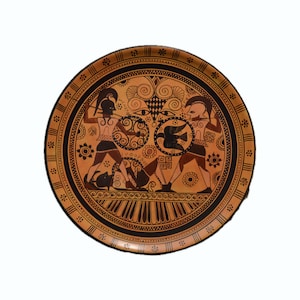 May include: A black and white ceramic plate with a circular design. The center of the plate features a scene of two figures in black and white, with a bird in the center. The plate has a brown background.