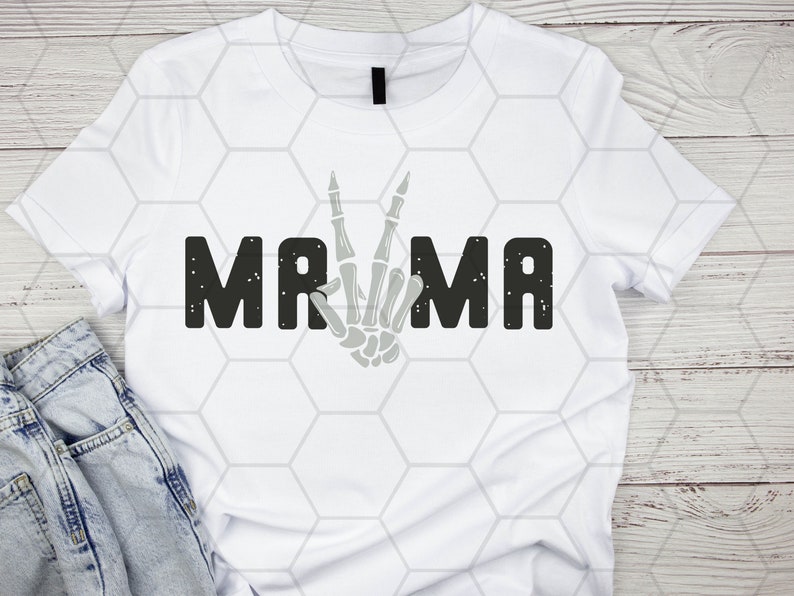 Puede incluir: Camiseta blanca con un gr&aacute;fico negro que dice "MAMA" con una mano de esqueleto haciendo un signo de paz en el medio de la palabra.