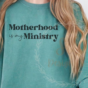 May include: A teal sweatshirt with the text "Motherhood is my Ministry" printed in black.