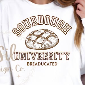 May include: White sweatshirt with brown text that reads "Sourdough University Breadeducated" and a drawing of a sourdough loaf of bread.