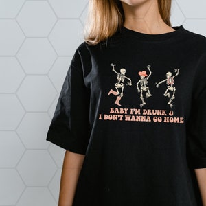 May include: Black t-shirt with a graphic of three skeletons dancing. The text "Baby I'm Drunk & I Don't Wanna Go Home" is printed below the skeletons.