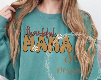 May include: Teal-colored sweatshirt with the words "thankful MAMA" in brown, red, and white. The word "thankful" is in a script font, and the word "MAMA" is in a bubble font. Small daisy flowers are placed on the letters.