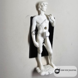 May include: A white plastic light switch cover shaped like a statue of a nude man. The switch cover is mounted on a wall. The text "Don't Stop Collecting" is visible in the lower right corner of the image.