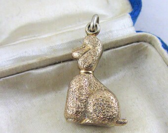 May include: A gold-colored poodle charm in a blue velvet jewelry box. The box has a white label with the text "Diamond Merchant & Goldsmith Chas. D. Allen 61 Lord St. Southport."