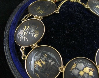 Op de afbeelding: Een gouden armband met zwarte emaille medaillons met ingewikkelde gouden ontwerpen. De armband zit in een blauwe fluwelen doos met de inscriptie "J.W. Benson Ludgate Hill London."