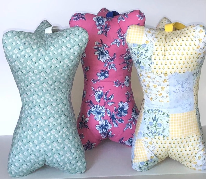 May include: Three decorative dress forms in a row. The forms are made of fabric with floral patterns. One is light blue with white flowers, one is pink with blue flowers, and the third is yellow with blue and white floral patches.