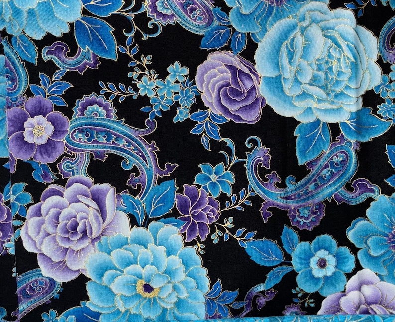 May include: Close-up of a fabric with a floral pattern. The design features large blue and purple flowers, paisley shapes, and gold accents on a black background. The flowers include roses and other detailed blooms.