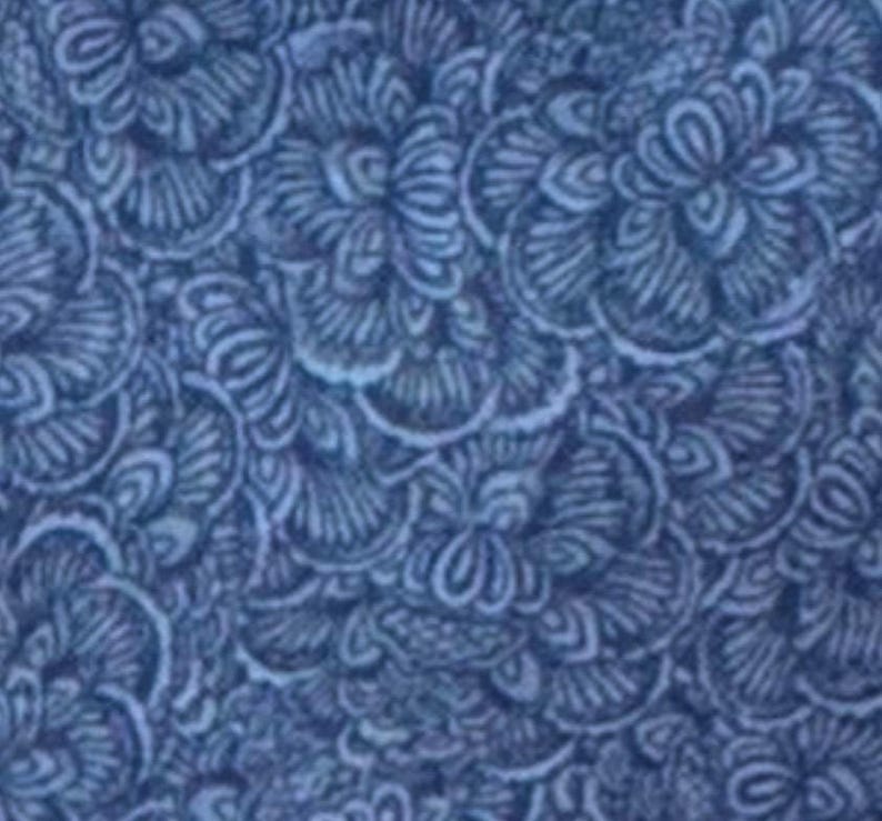May include: A close-up of a fabric with a repeating floral pattern in shades of blue. The design features stylized, swirling flower-like shapes with intricate details, creating a textured appearance. The overall effect is a dense, all-over print.