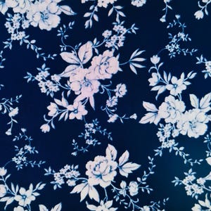 May include: Dark navy blue fabric with a repeating floral pattern. The design features white and light blue flowers of various sizes, including roses and smaller blossoms, with delicate stems and leaves.