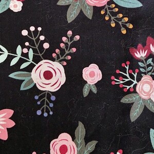 May include: Close-up of a black fabric with a floral pattern. The design features various flowers in shades of pink and red, with green leaves and small blue and yellow accents. The flowers are arranged in a scattered pattern.
