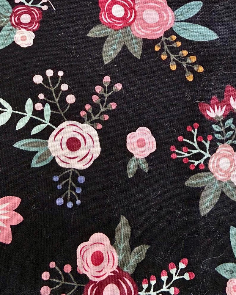 May include: Close-up of a black fabric with a floral pattern. The design features various flowers in shades of pink and red, with green leaves and small blue and yellow accents. The flowers are arranged in a scattered pattern.
