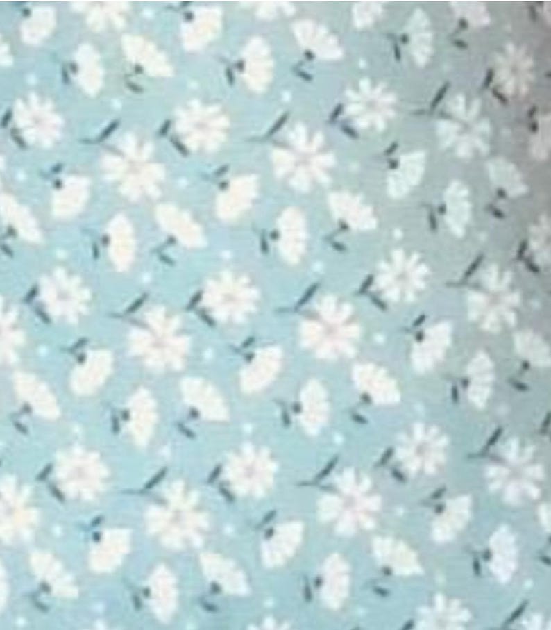 May include: A light blue fabric with a repeating pattern of white flowers and leaves. The flowers have multiple petals and are interspersed with smaller, fan-shaped elements. The background has small white dots.