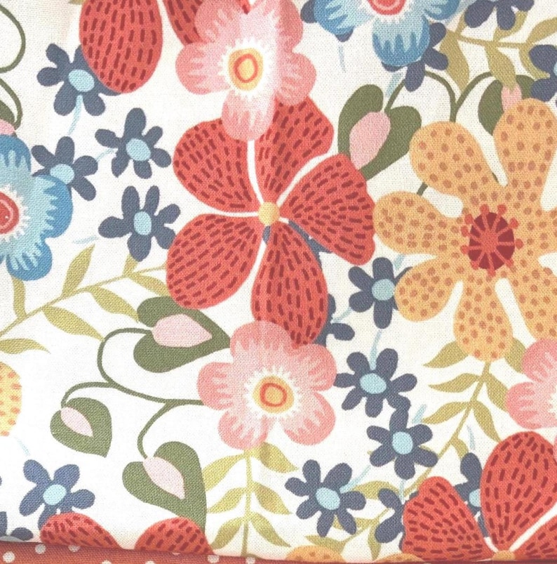 May include: Floral fabric with a white background, featuring large red, pink, and orange flowers. Smaller blue and pink flowers are scattered throughout, with green leaves and stems. The fabric has a dotted border.