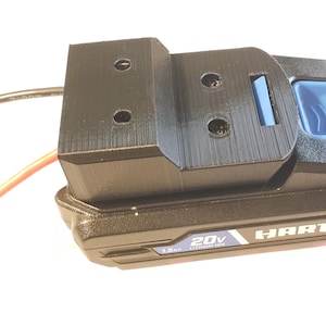 May include: A black 3D-printed adapter attached to a black and blue 20V HART battery. The adapter has three holes and a blue button. Wires extend from the adapter. The battery is labeled "20V" and "Lithium-Ion".