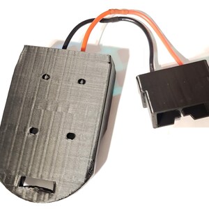 May include: A 3D printed black plastic battery holder with four holes and a cutout on the bottom. The holder is connected to a black plastic connector with two wires, one orange and one black.