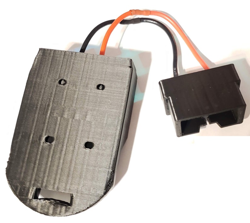 May include: A 3D printed black plastic battery holder with four holes and a cutout on the bottom. The holder is connected to a black plastic connector with two wires, one orange and one black.