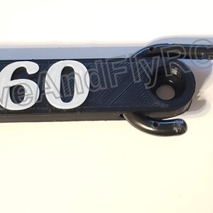 Puede incluir: Gancho de pl&aacute;stico negro con el n&uacute;mero "660" impreso en blanco. Un cord&oacute;n rojo est&aacute; unido al gancho.