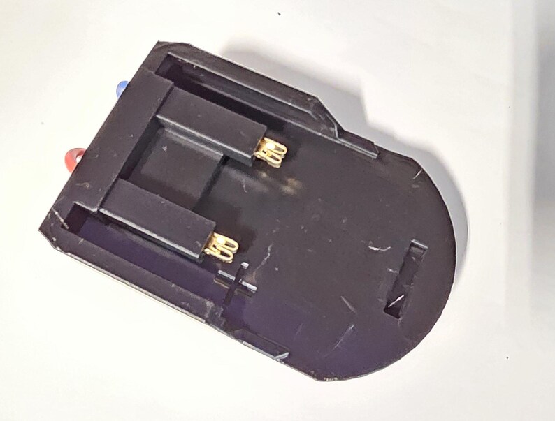 K&ouml;nnte beinhalten: Schwarzer Batteriehalter aus Kunststoff mit zwei goldfarbenen Kontakten. Der Halter hat ein rotes und ein blaues Kabel.