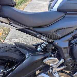 Puede incluir: Una motocicleta negra con un asiento plateado y un motor negro y plateado. La motocicleta tiene un guardabarros trasero negro con un ribete plateado y el n&uacute;mero "660" impreso en &eacute;l.