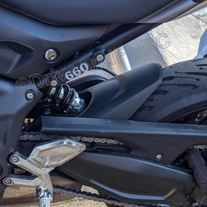 Puede incluir: Primer plano de una motocicleta negra con una cadena plateada y un guardabarros negro. La motocicleta tiene un amortiguador negro con un resorte plateado. El texto "@Drive660" es visible en el guardabarros.