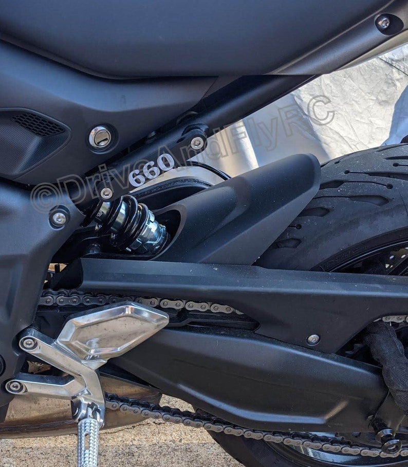 Puede incluir: Primer plano de una motocicleta negra con una cadena plateada y un guardabarros negro. La motocicleta tiene un amortiguador negro con un resorte plateado. El texto "@Drive660" es visible en el guardabarros.