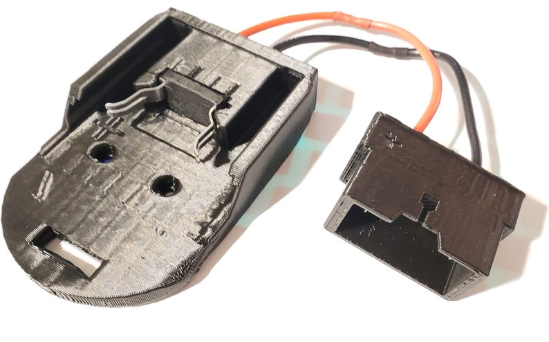 May include: A 3D printed battery adapter with a black plastic housing and a red and black wire. The adapter has a connector on one end and a battery holder on the other end.