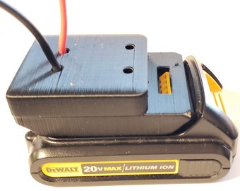 May include: A black 3D printed battery adapter for a DeWalt 20V Max Lithium Ion battery. The adapter has two holes for wires and a yellow connector.