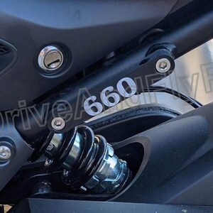 Puede incluir: Primer plano de una motocicleta negra con una pegatina plateada con el n&uacute;mero "660" en el basculante.