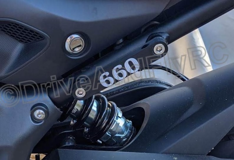 Puede incluir: Primer plano de una motocicleta negra con una pegatina plateada con el n&uacute;mero "660" en el basculante.