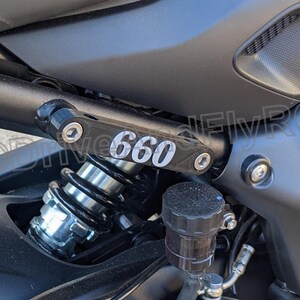 Puede incluir: Primer plano de una motocicleta con un amortiguador negro y plateado y un soporte de metal negro con el n&uacute;mero "660" impreso en &eacute;l.