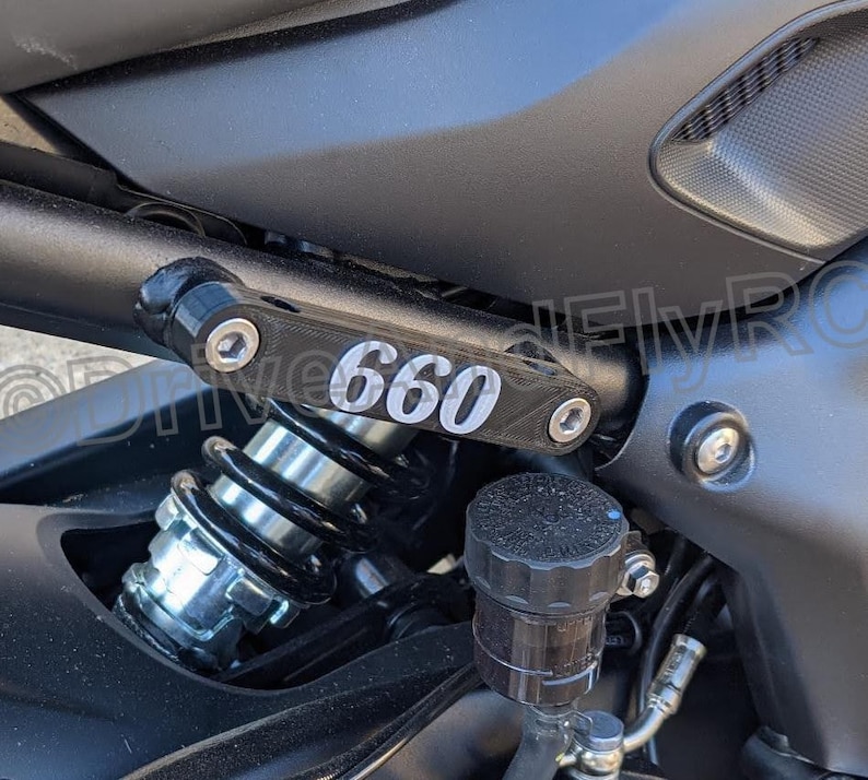 Puede incluir: Primer plano de una motocicleta con un amortiguador negro y plateado y un soporte de metal negro con el n&uacute;mero "660" impreso en &eacute;l.