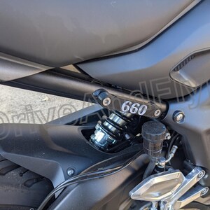 Puede incluir: Primer plano de una motocicleta negra con un guardabarros trasero negro y un amortiguador plateado. La motocicleta tiene una placa negra con el n&uacute;mero "660" impreso en ella.