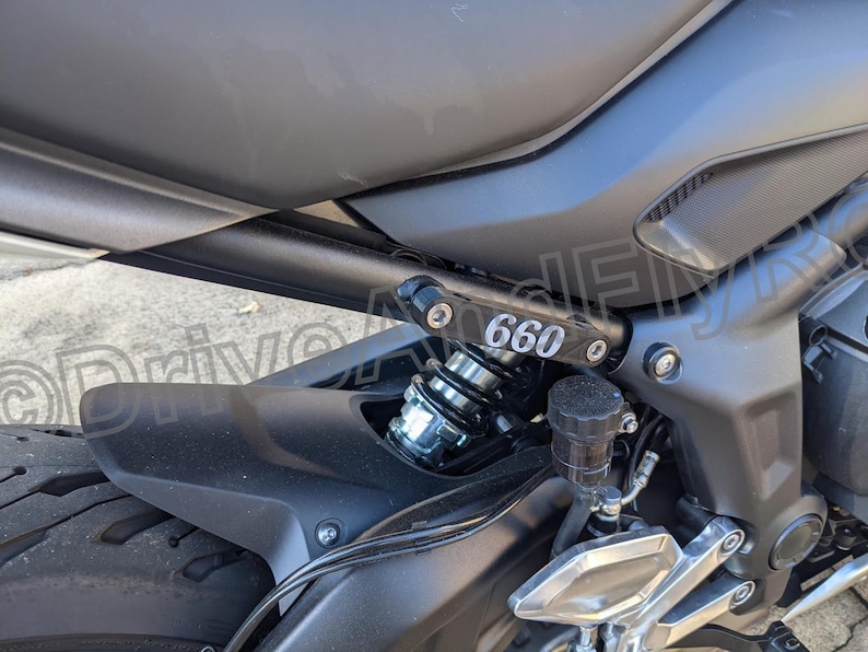 Puede incluir: Primer plano de una motocicleta negra con un guardabarros trasero negro y un amortiguador plateado. La motocicleta tiene una placa negra con el n&uacute;mero "660" impreso en ella.