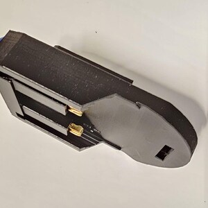 K&ouml;nnte beinhalten: Ein schwarzer Batteriehalter aus Kunststoff mit zwei vergoldeten Kontakten. Der Halter hat einen blauen Knopf oben.