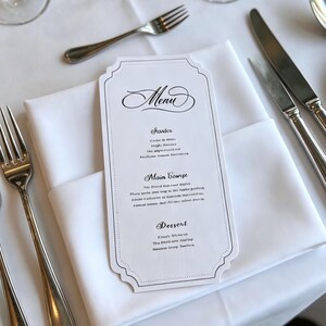 Może przedstawiać: Formalne nakrycie stołu z białym obrusem, sztućcami i kartą menu. Karta menu jest biała z czarnym tekstem i ozdobną obwódką. Obecne są również kieliszki do wina i złożone serwetki.