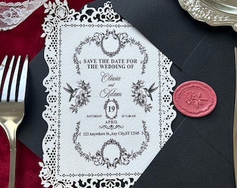 May include: A wedding invitation with a black envelope and a white, laser-cut decorative border. The invitation card reads "Save the Date for the Wedding of Olivia and Adam" with the date April 19th. A pink wax seal and a silver fork and knife are also present.