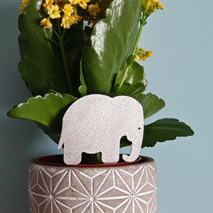 May include: A potted succulent plant with yellow flowers in a geometric patterned grey planter with a white elephant figurine.