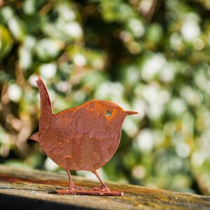 Side view of weathered steel wren fence topper captured atop a log edge, emphasising its graceful beak, tail and cut-out details. This artisan rusty metal bird décor is designed to embrace the elements and develop a unique patina over time. Ideal for cottage gardens, pergolas and porch displays; a tasteful nod to beloved British garden birds and nature-led design.